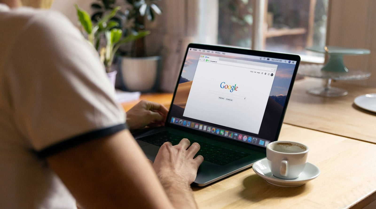 Person searching mattresses on google on their MacBook with a cup of coffee on the table.