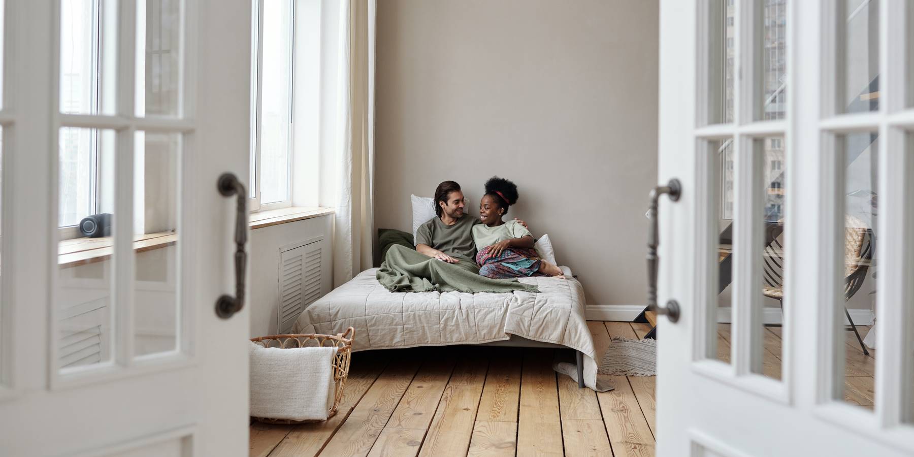 A couple lying in bed with doors open in bedroom with hardwood floors