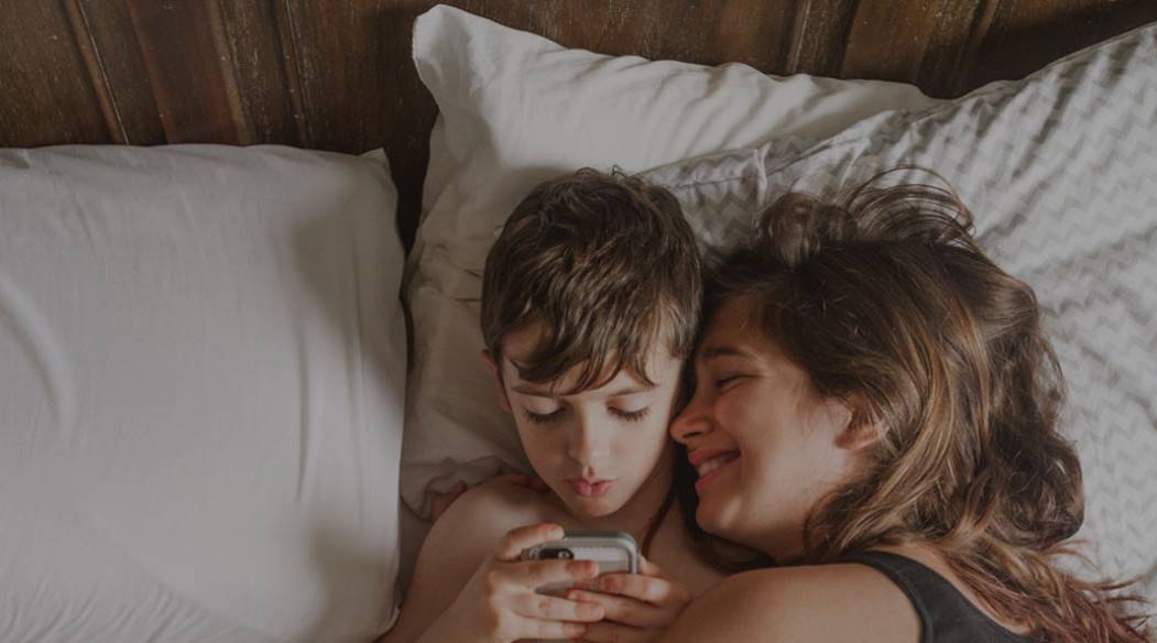 Mother and son lying in bed looking at an iphone.