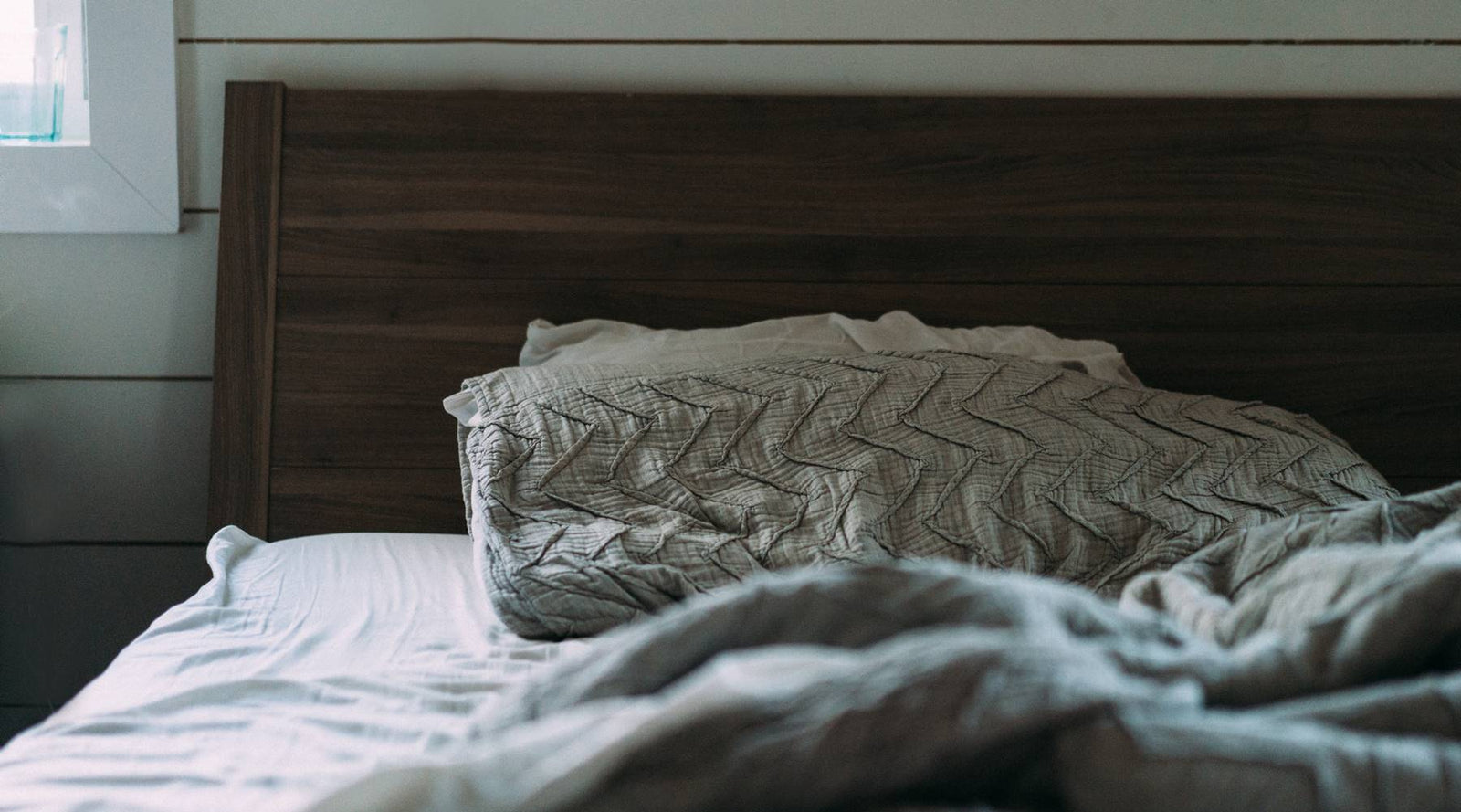 Unmade bed with gray pillow and green comforter on dark wood bed frame.