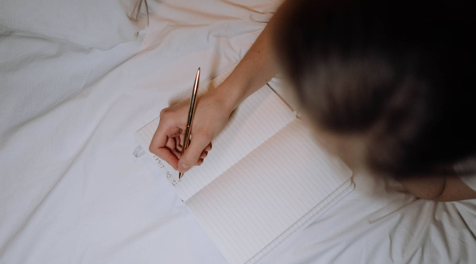 Women writing to do list on a bed with white sheets.
