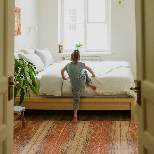 Girl climbing into new latex mattress with white sheets and pillows on a wood platform and the window open.