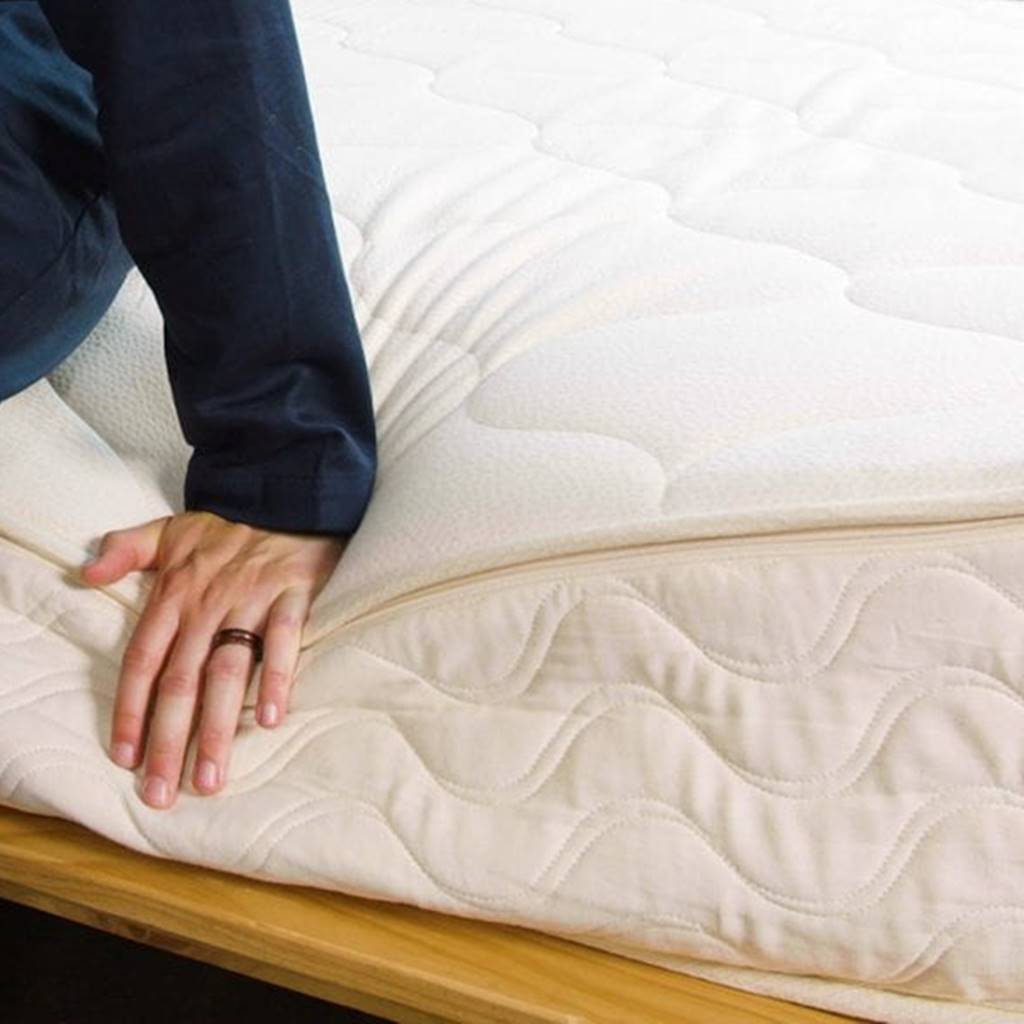 Hand with wedding band pushing on the edge of a latex mattress