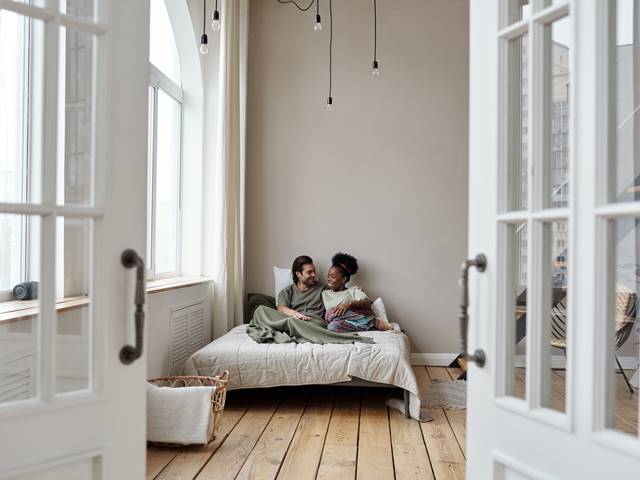 A couple lying in bed with doors open in bedroom with hardwood floors