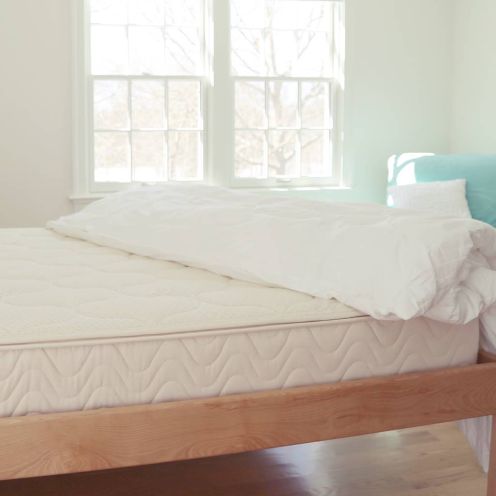 Spindle mattress on wood platform bed with a white comforter and a blue chair in the background.