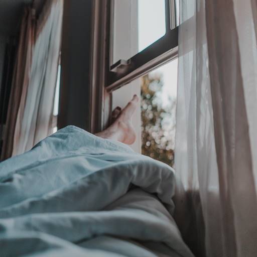 Person lying in bed with feet sticking out of white blanket with window open.