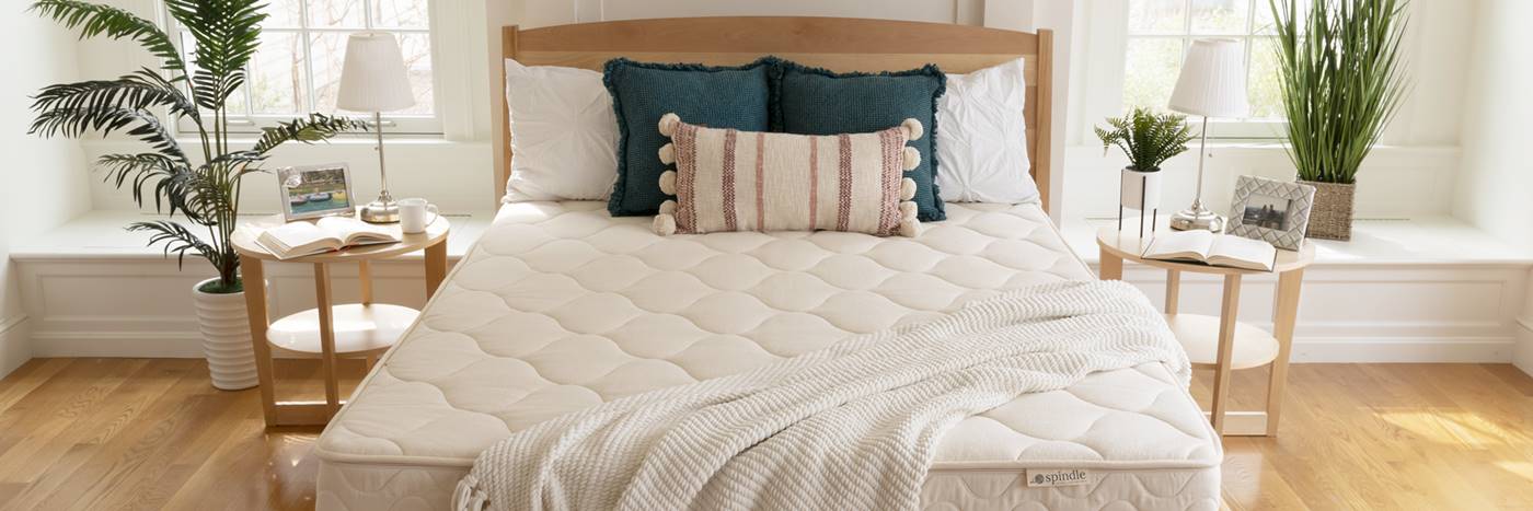 Spindle latex mattress with pillows uncover on wood bedframe with windows in the background.