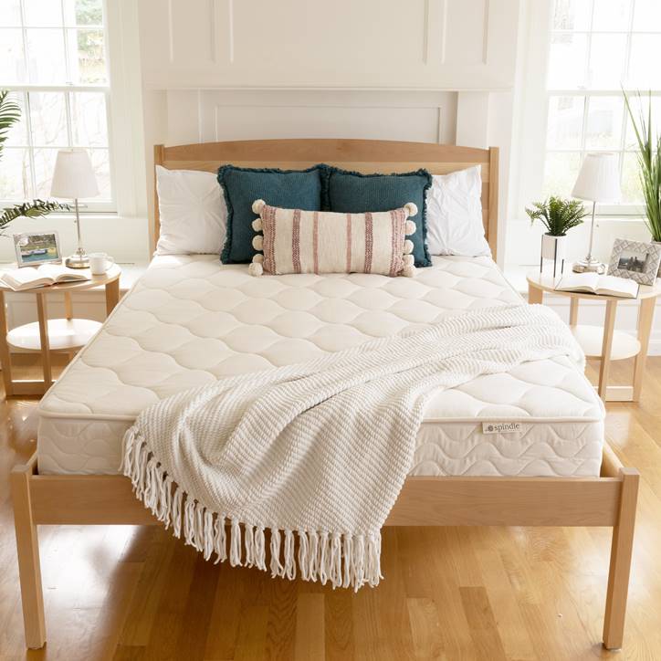 Spindle Mattress with pillows and white blanket on wood platform bed.